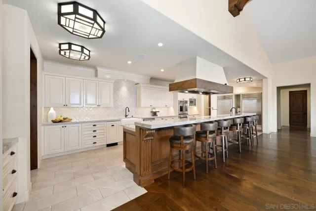 a kitchen with stainless steel appliances kitchen island granite countertop a refrigerator a stove and white cabinets with wooden floor