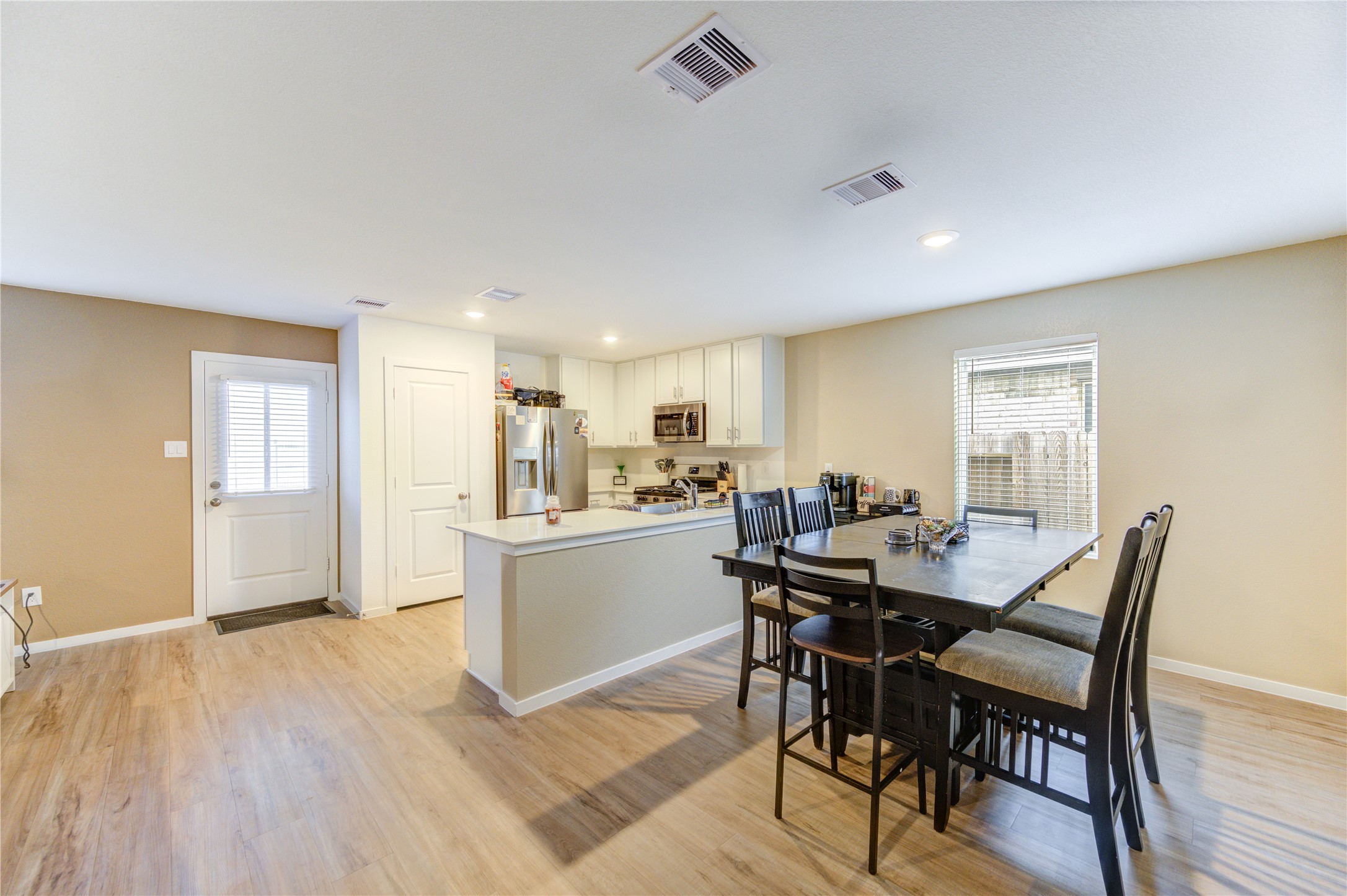 1111 Rustic Willow Drive Beasley, TX 77417 - Photo 11 of 42 This photo showcases a bright, open-concept kitchen and dining area with modern appliances, white cabinetry, and vinyl plank flooring. The space features a large dining table, ample natural light from a window, and convenient access through a side door.