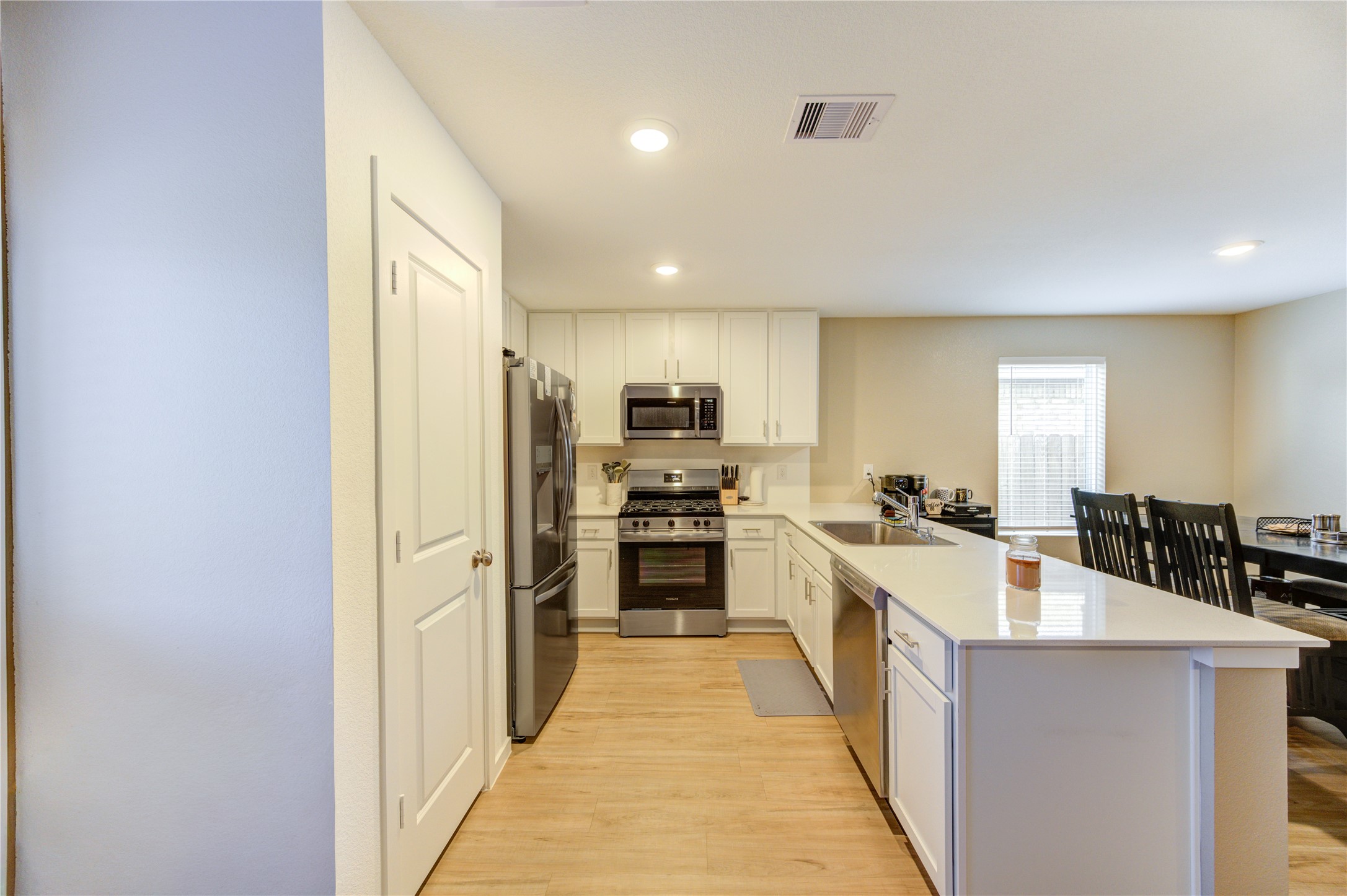 1111 Rustic Willow Drive Beasley, TX 77417 - Photo 14 of 42 This kitchen features modern stainless steel appliances, white cabinetry, and a spacious island with a sink. The open layout flows into a cozy dining area with natural light from a large window.