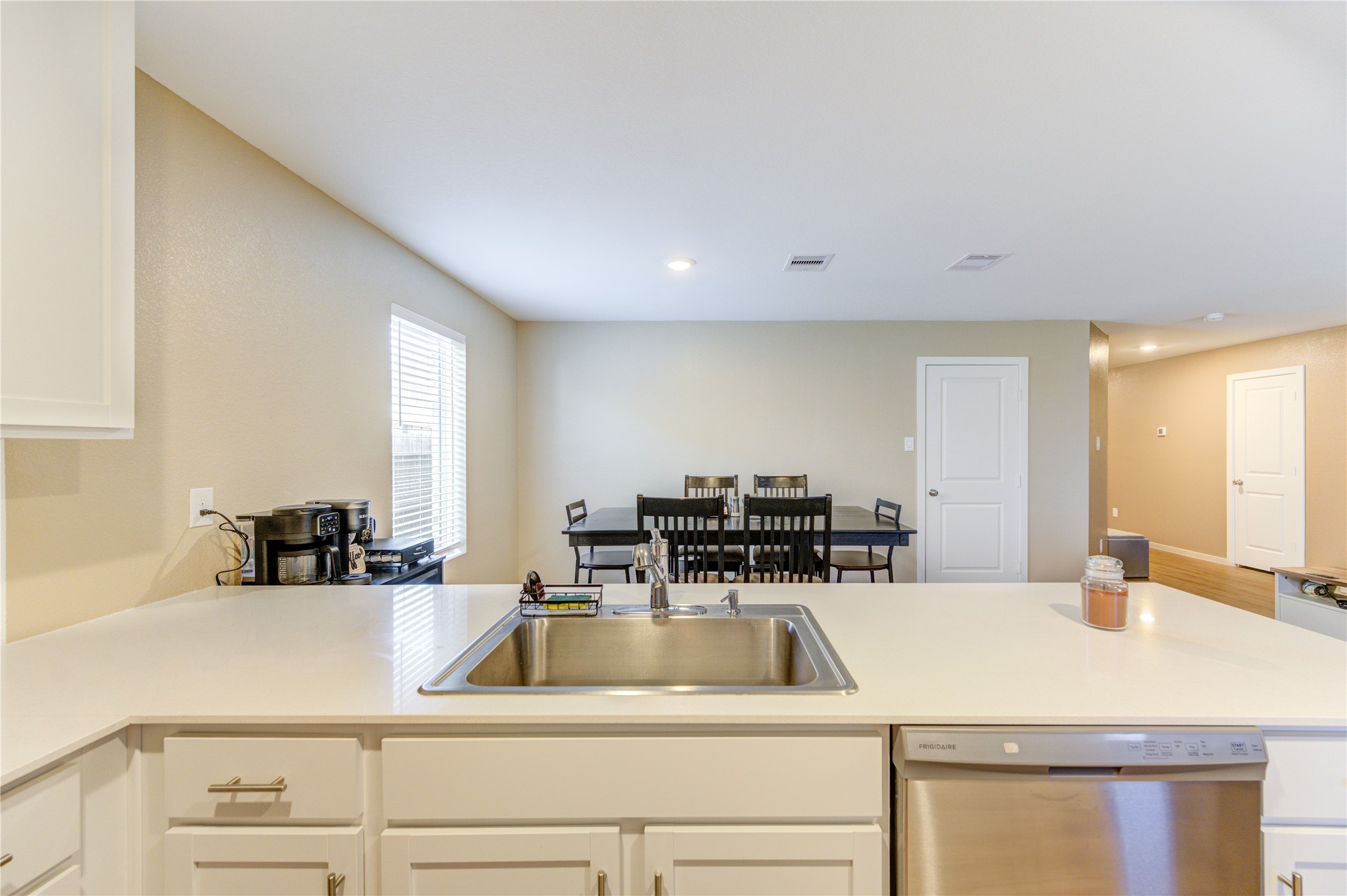 1111 Rustic Willow Drive Beasley, TX 77417 - Photo 16 of 42 This photo showcases a bright, open kitchen with a modern design featuring a central island with a sink and dishwasher. It leads into a dining area with ample natural light, neutral walls, and recessed lighting, creating a welcoming space.