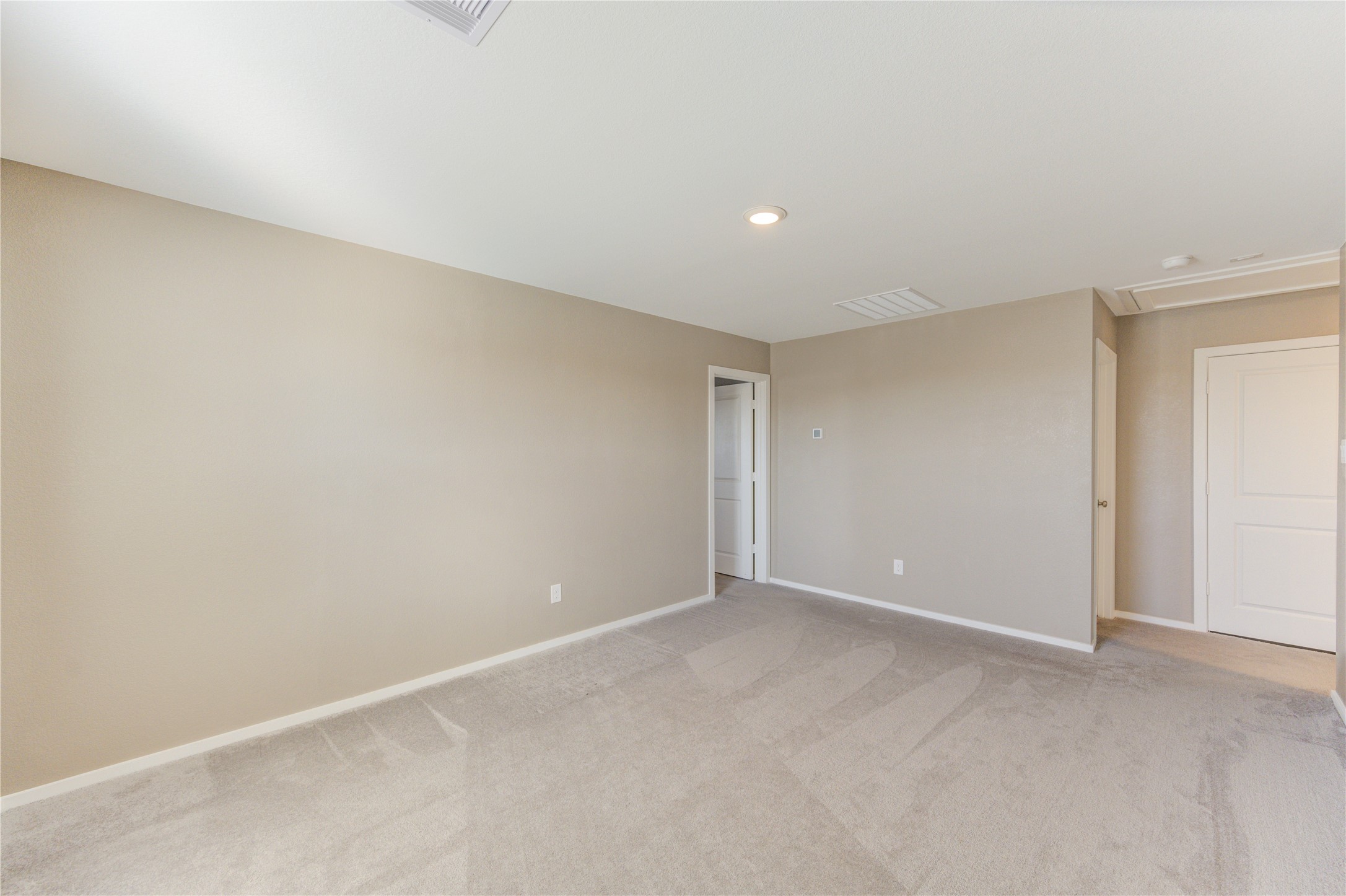 1111 Rustic Willow Drive Beasley, TX 77417 - Photo 20 of 42 This photo shows a spacious, carpeted room with neutral-colored walls and ceiling. It features recessed lighting and leads to a hallway with white doors, offering a clean and versatile space.