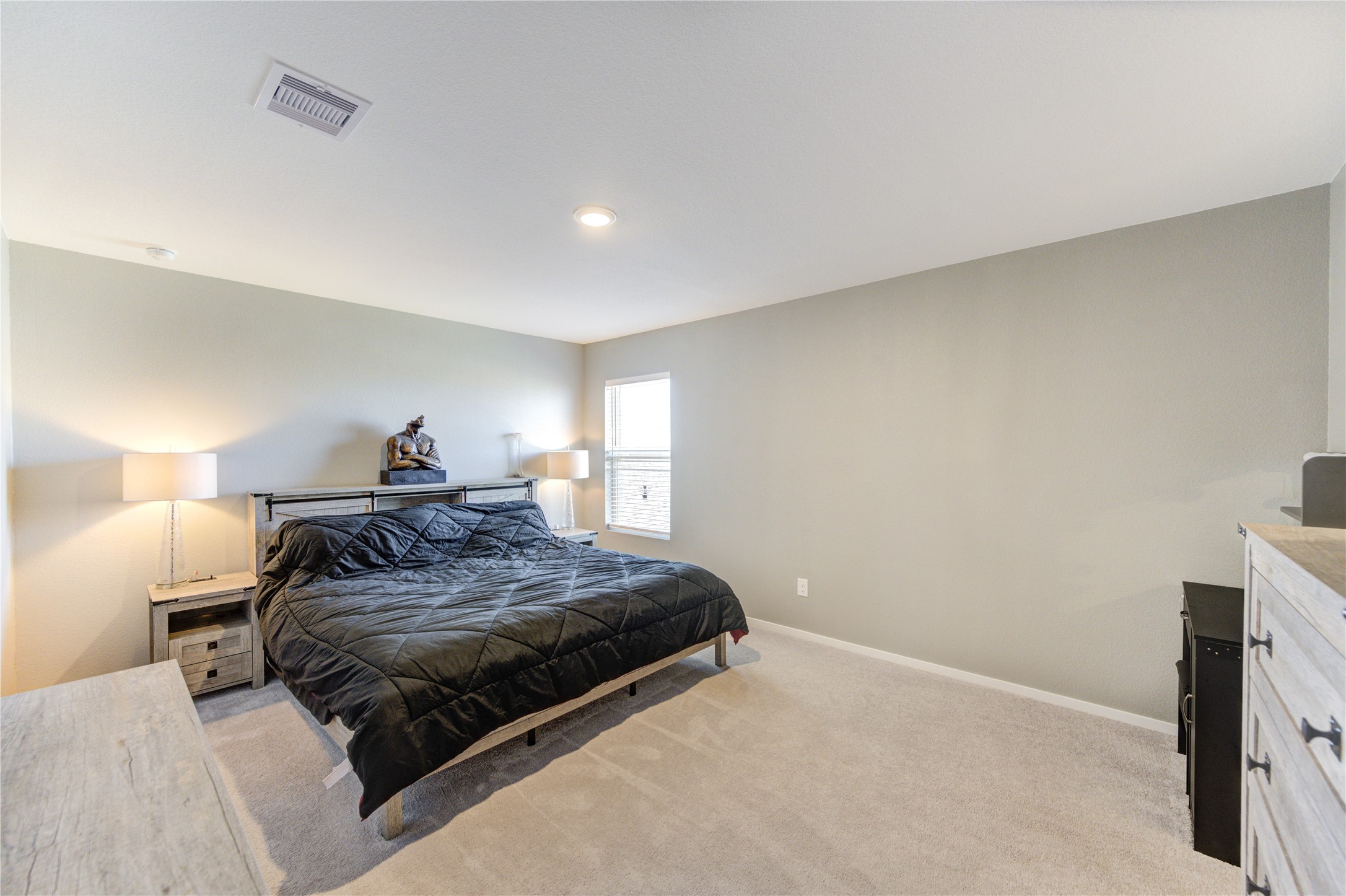 1111 Rustic Willow Drive Beasley, TX 77417 - Photo 27 of 42 This spacious bedroom features neutral walls, carpeted flooring, and ample natural light from a large window. It includes a modern bed, side tables with lamps, and a dresser, offering a cozy and inviting atmosphere.