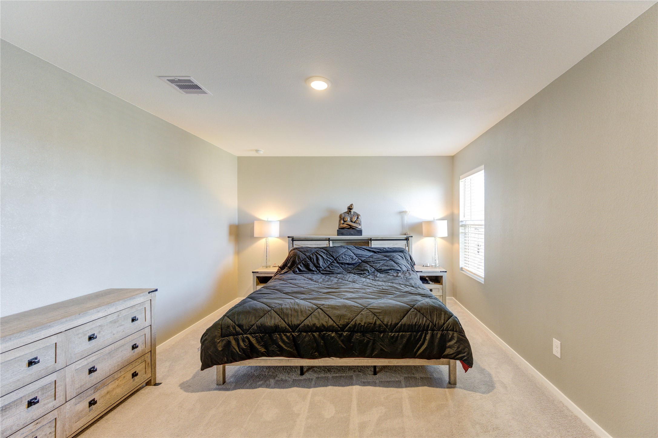 1111 Rustic Willow Drive Beasley, TX 77417 - Photo 28 of 42 This spacious bedroom features neutral walls and carpeting, a comfortable bed with side tables and lamps, and a large window providing natural light. A dresser offers additional storage.
