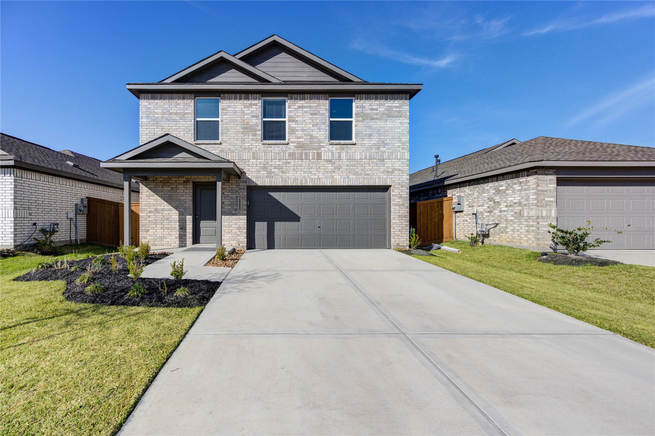 1111 Rustic Willow Drive Beasley, TX 77417 - Photo 3 of 42 This photo showcases a modern two-story brick home with a clean, gray garage door and a neatly landscaped front yard. The driveway is spacious, leading to a welcoming entryway. The house is set in a suburban neighborhood under a clear blue sky.