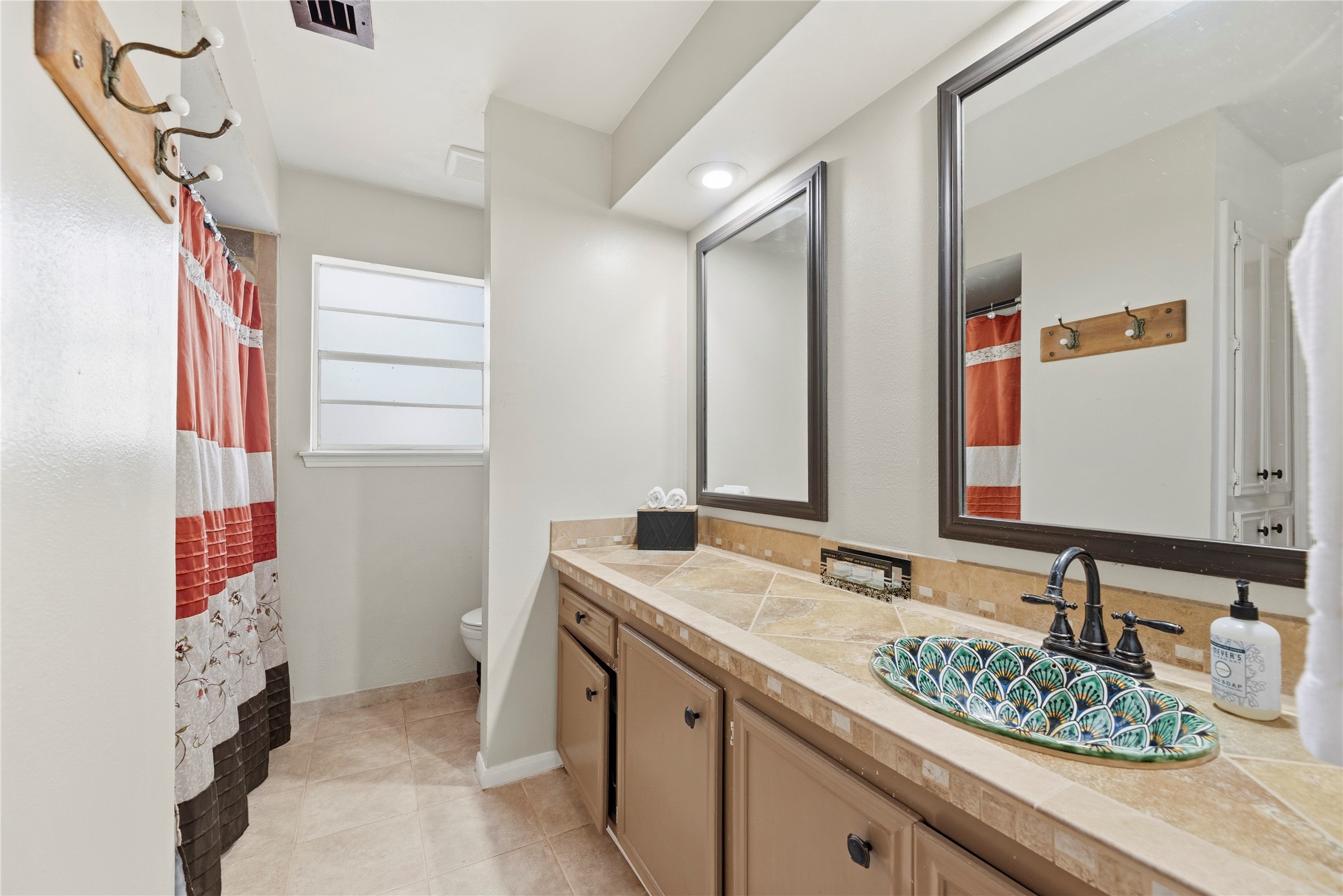 14203 Wickersham Lane Houston, TX 77077 - Photo 13 of 25 Primary bath boasting an extended vanity counter surfaced in warm stone tiles, dual matching mirrors, an ornate painted vessel sink, and a layout that offers separate privacy areas.