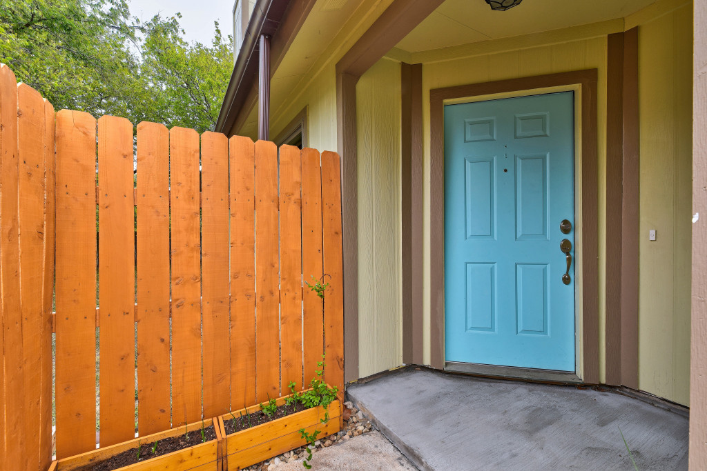 6002 Baton Rouge Drive Austin, TX 78727 - Photo 3 of 20 Vibrant blue six-panel entry door with brass hardware, set against a light yellow exterior with brown trim
