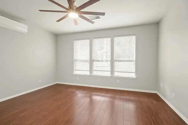 an empty room with wooden floor fan and windows