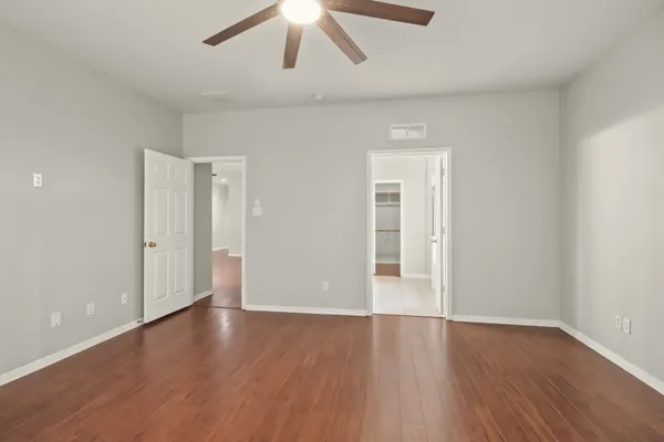 a view of an empty room with wooden floor and a ceiling fan