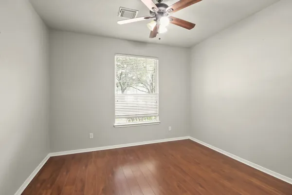an empty room with wooden floor chandelier fan and windows