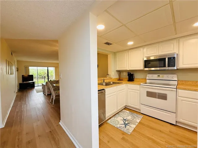 a kitchen with stainless steel appliances a stove a sink dishwasher a refrigerator white cabinets and wooden floor