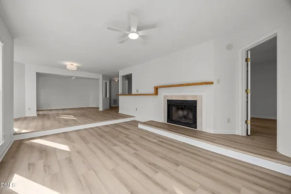 a view of an empty room with wooden floor fireplace and a window