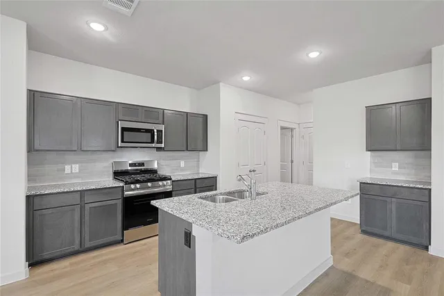 a kitchen with stainless steel appliances granite countertop a stove top oven a sink and dishwasher a refrigerator with wooden floor