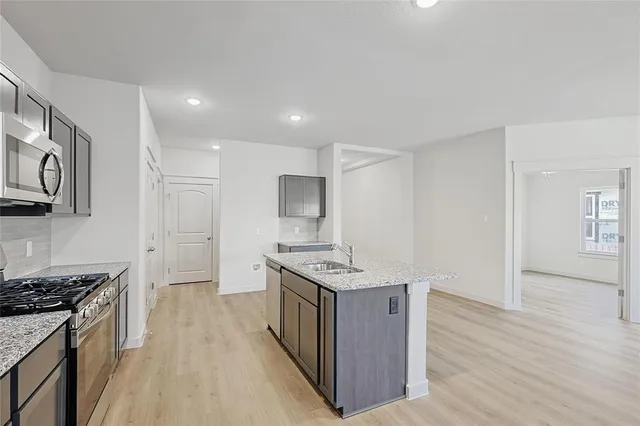 a kitchen with stainless steel appliances granite countertop a stove top oven a sink dishwasher and a refrigerator with wooden floor