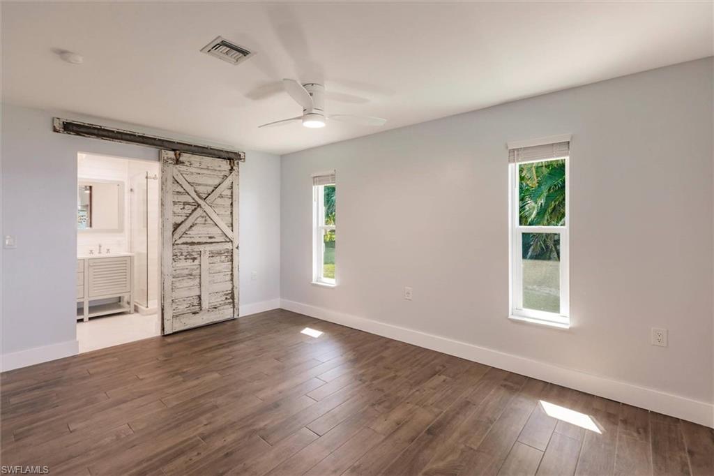 138 Riverview Road Fort Myers, FL 33905 - Photo 25 of 50 Spare room featuring a barn door, dark wood-type flooring, a ceiling fan, and baseboards