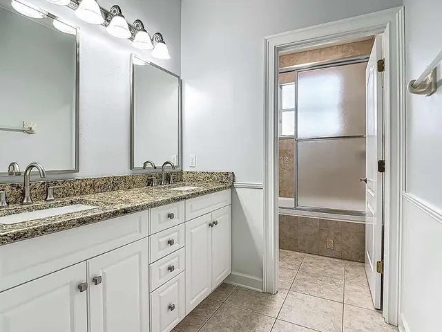 a bathroom with a granite countertop sink two mirror and a shower