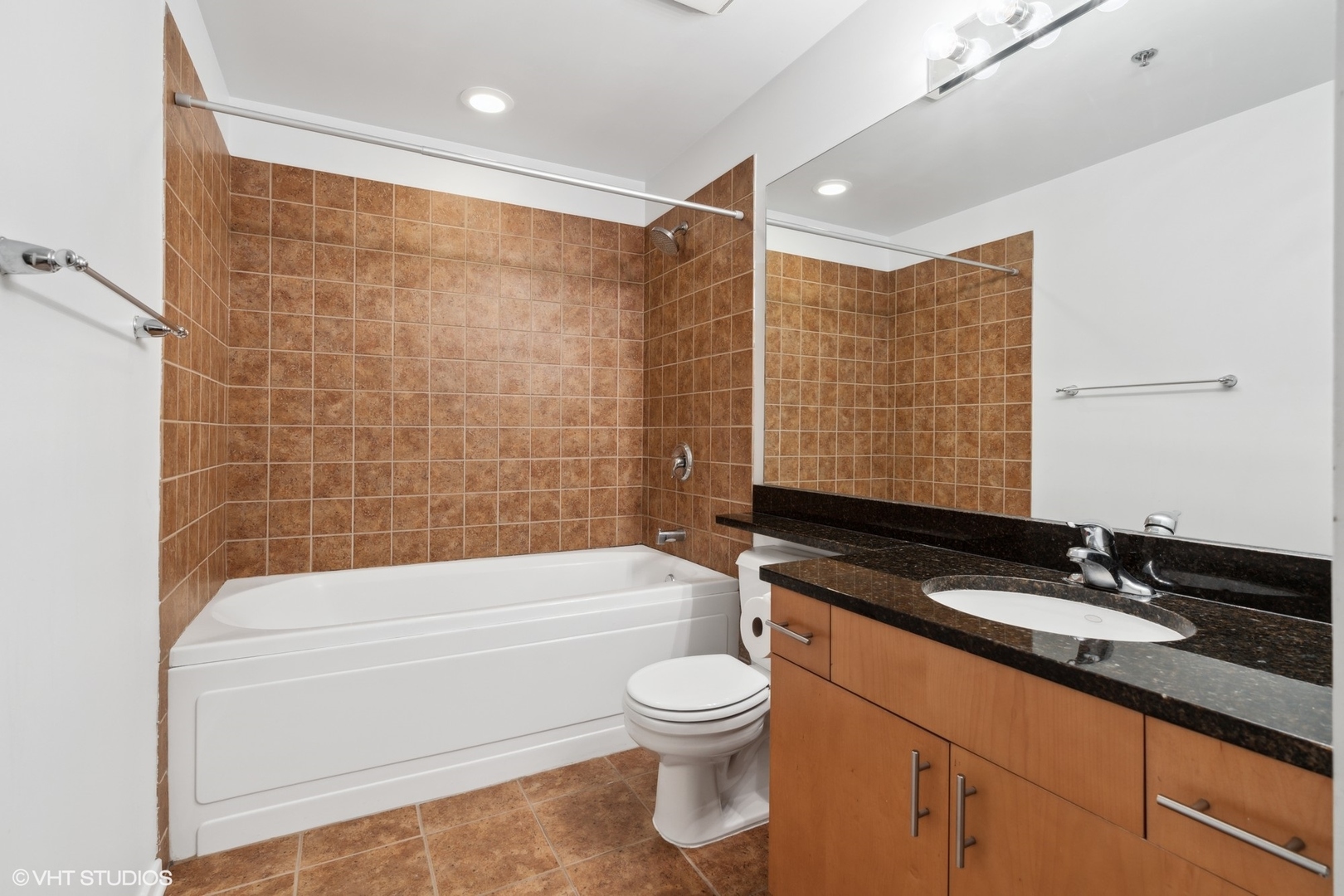 1040 West Adams Street, Unit 107 Chicago, IL 60607 - Photo 11 of 14 a bathroom with a granite countertop toilet a sink a mirror a bathtub and shower