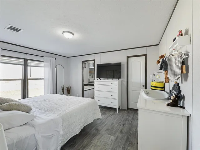 a bedroom with a bed a flat tv screen and a dresser