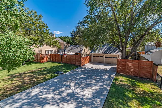 a view of a backyard with wooden fence and large trees