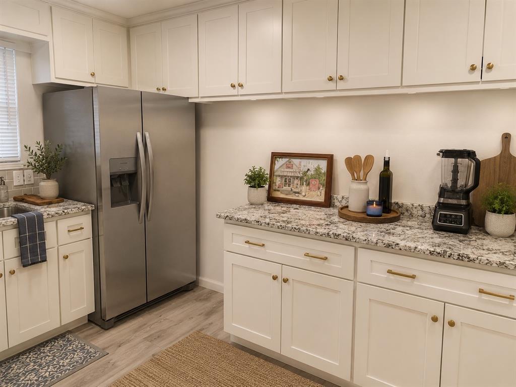 1109 North Howeth Street Gainesville, TX 76240 - Photo 3 of 11 White shaker-style cabinetry with gold hardware, stainless steel side-by-side refrigerator, speckled granite countertops, wood-finish flooring, and recessed lighting