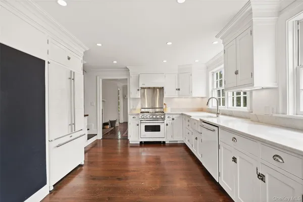 a large white kitchen with a stove top oven a refrigerator a sink and dishwasher with wooden floor