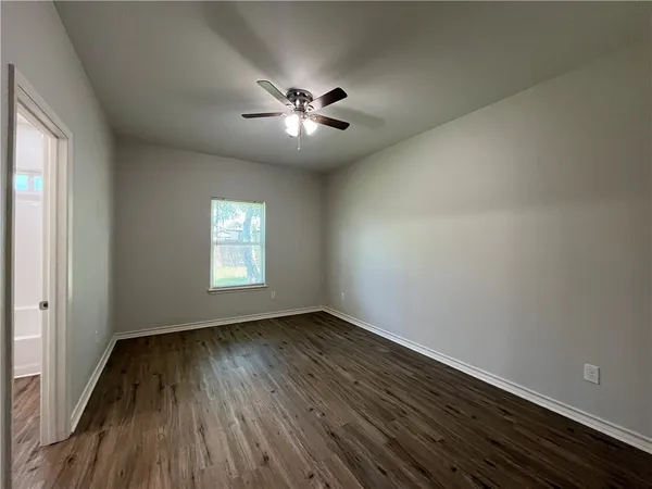 an empty room with wooden floor chandelier fan and windows