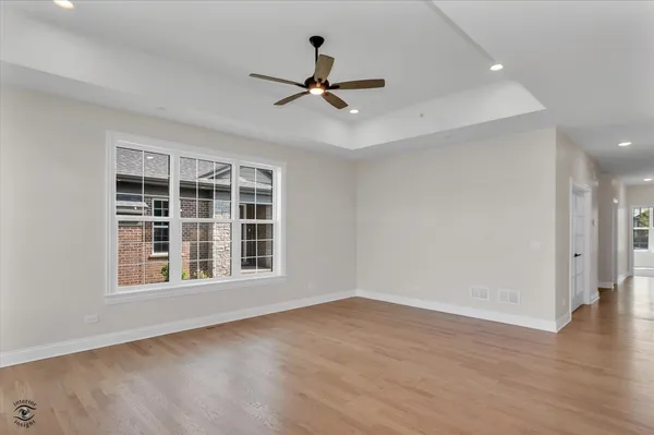 a view of an empty room with wooden floor ceiling fan and window