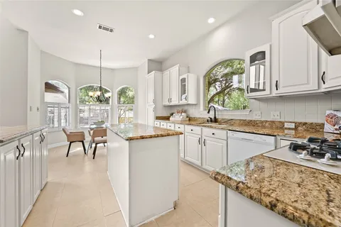 a kitchen with stainless steel appliances granite countertop a stove top oven a sink a dining table and chairs with wooden floor