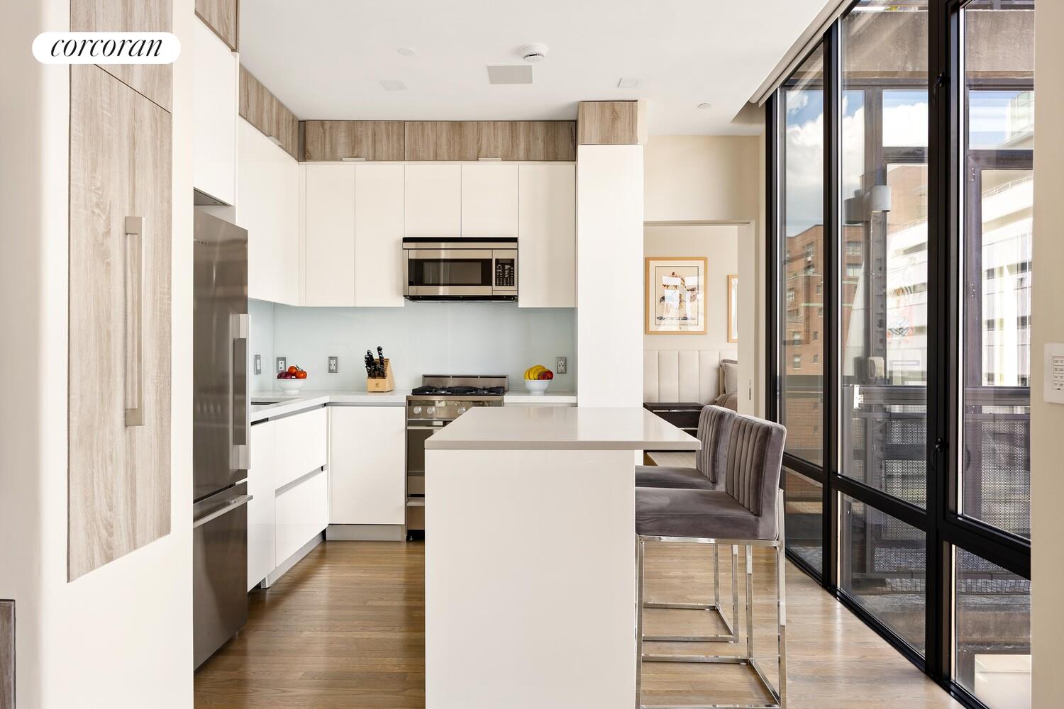 148 East 24th Street, Unit 15A Manhattan, NY 10010 - Photo 4 of 14 a kitchen with kitchen island wooden cabinets and refrigerator