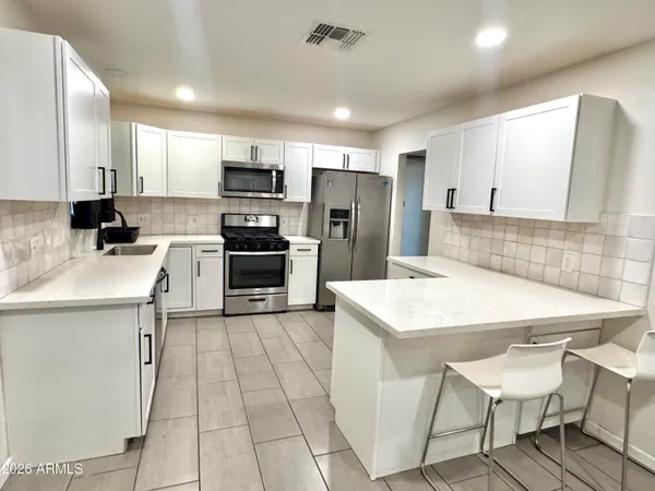 a kitchen with stainless steel appliances a stove top oven refrigerator a sink a dining table and chairs
