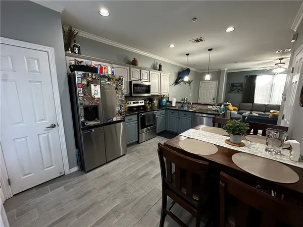 a kitchen with stainless steel appliances kitchen island granite countertop a refrigerator a sink dishwasher a dining table and chairs with wooden floor