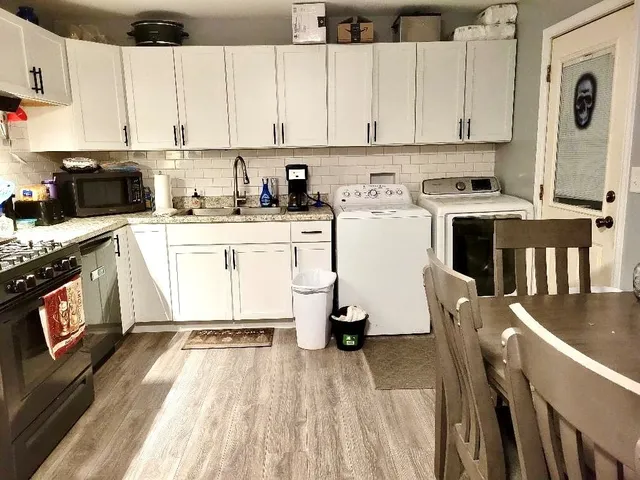 a kitchen with stainless steel appliances granite countertop a stove a sink dishwasher and white cabinets with wooden floor