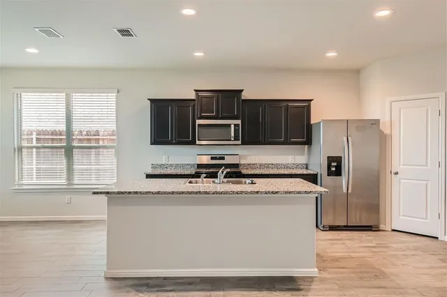 a kitchen with stainless steel appliances granite countertop a stove a sink and a refrigerator with wooden floor