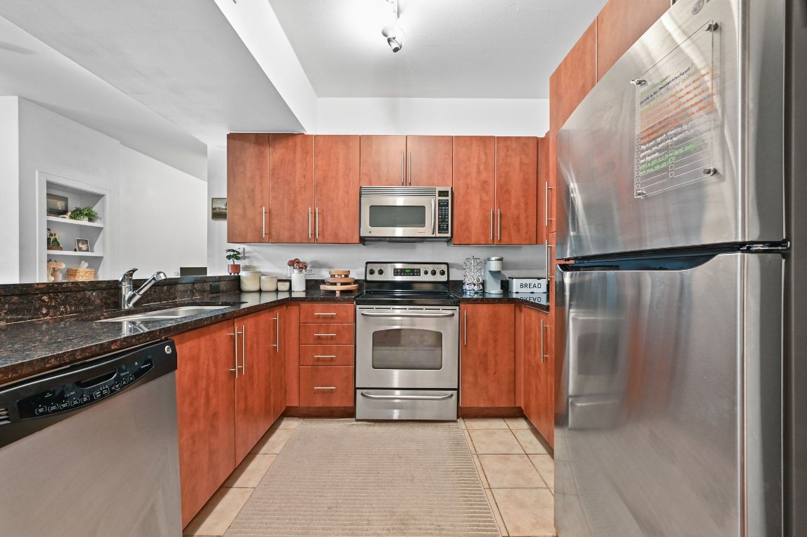 54 Rainey Street, Unit 416 Austin, TX 78701 - Photo 3 of 40 Kitchen featuring appliances with stainless steel finishes, dark stone countertops, light tile patterned flooring, and brown cabinets