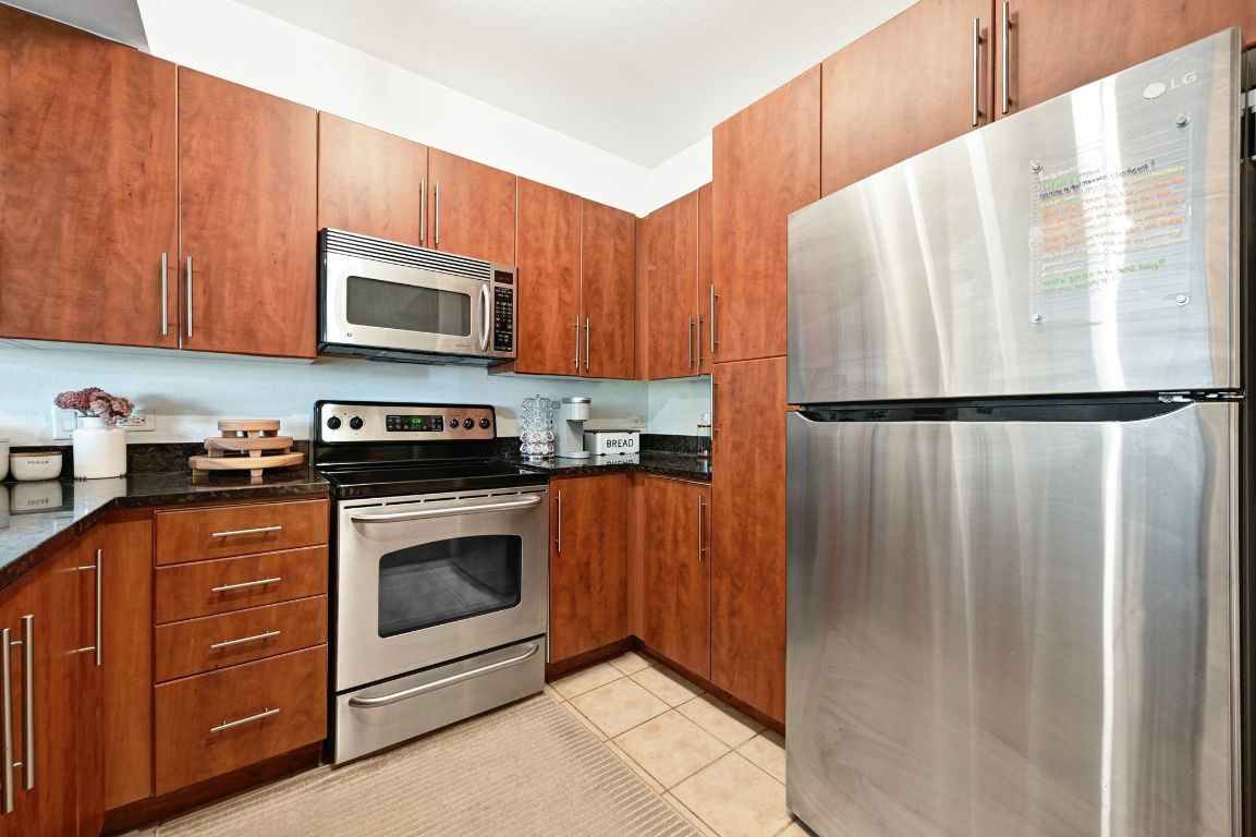 54 Rainey Street, Unit 416 Austin, TX 78701 - Photo 5 of 40 Kitchen with appliances with stainless steel finishes, dark stone counters, light tile patterned floors, and brown cabinets
