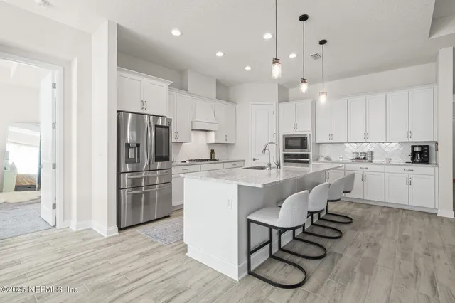 a kitchen with stainless steel appliances granite countertop a refrigerator a stove microwave and white cabinets with wooden floors