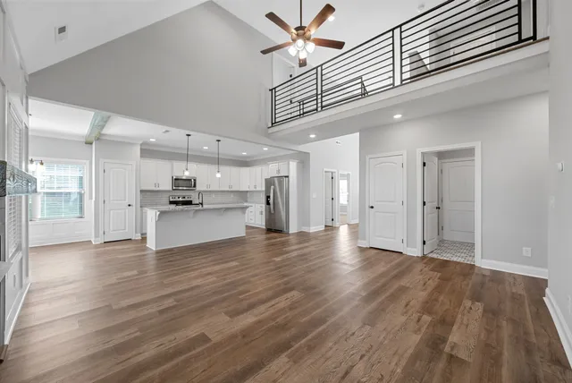a view of an empty room and kitchen view with wooden floor