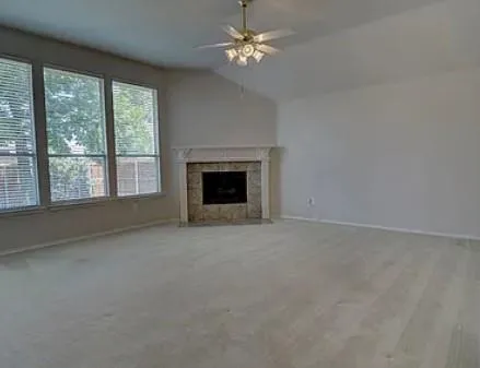 an empty room with chandelier fan and windows