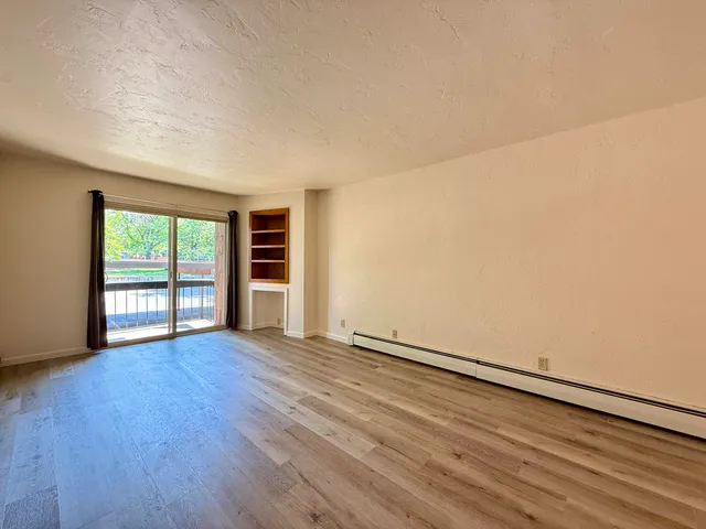 a view of an empty room with wooden floor and a window