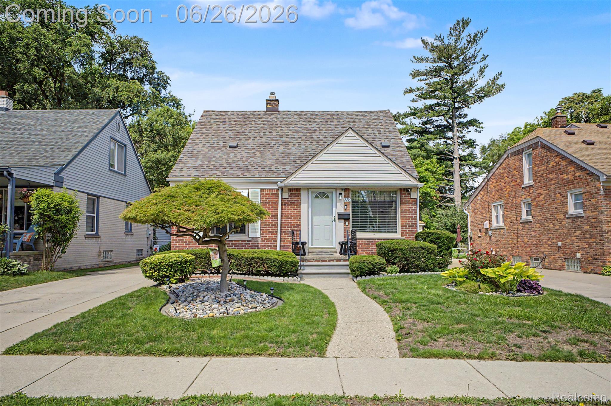 Brick and siding exterior featuring a covered front entry with white door, concrete walkway, and a manicured lawn with established landscaping