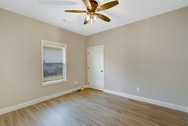 an empty room with wooden floor chandelier fan and windows