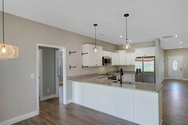 a kitchen with stainless steel appliances kitchen island granite countertop a sink a refrigerator and a wooden floor