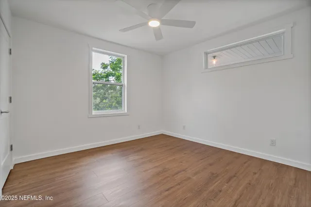 an empty room with wooden floor ceiling fan and windows