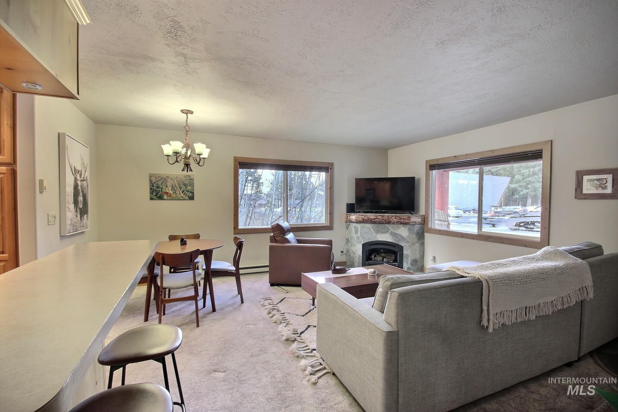 1000 Gamble Road McCall, ID 83638 - Photo 3 of 15 Living area featuring a premium fireplace, a textured ceiling, light carpet, a chandelier, and a baseboard heating unit