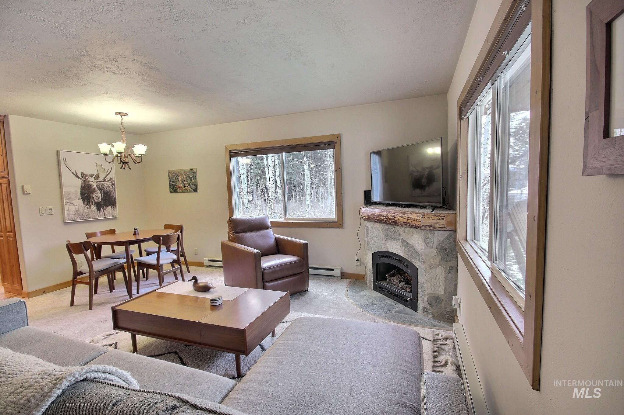 1000 Gamble Road McCall, ID 83638 - Photo 5 of 15 Living room with plenty of natural light, a tiled fireplace, a baseboard radiator, a chandelier, and a textured ceiling