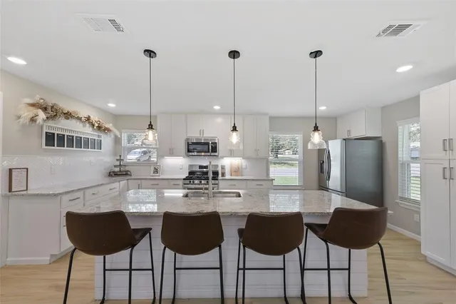 a kitchen with stainless steel appliances kitchen island granite countertop a refrigerator a stove a kitchen island with chairs and white cabinets