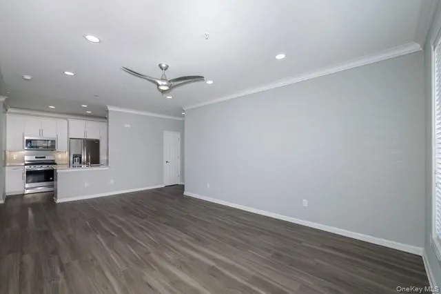 an empty room with wooden floor a ceiling fan a kitchen view and a ceiling fan