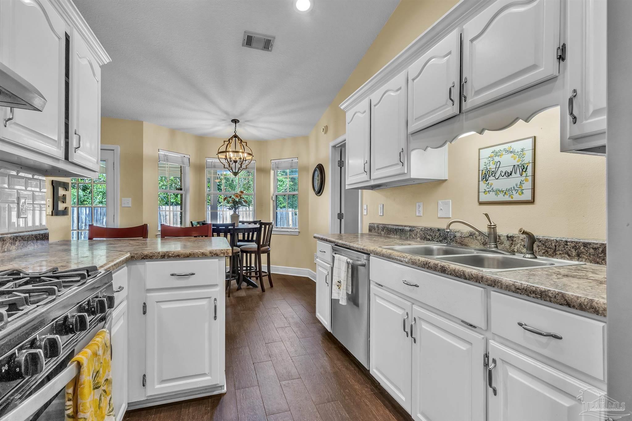 4321 Ridgeland Drive Pace, FL 32571 - Photo 10 of 36 a kitchen with stainless steel appliances granite countertop a stove a sink dishwasher and white cabinets with wooden floor