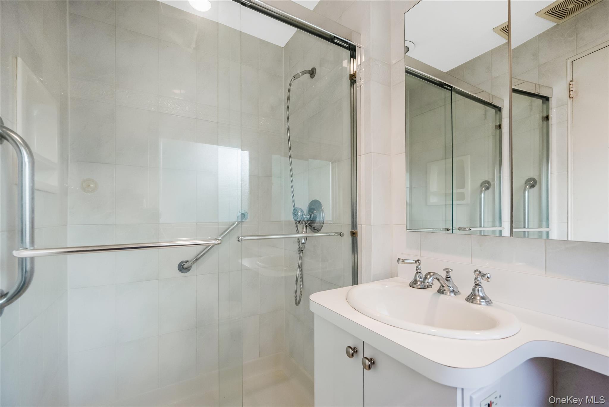 29 Randy Lane Plainview, NY 11803 - Photo 28 of 38 Glass-enclosed shower with ceramic tile surround, chrome fixtures, built-in medicine cabinet, and a vanity with a drop-in sink