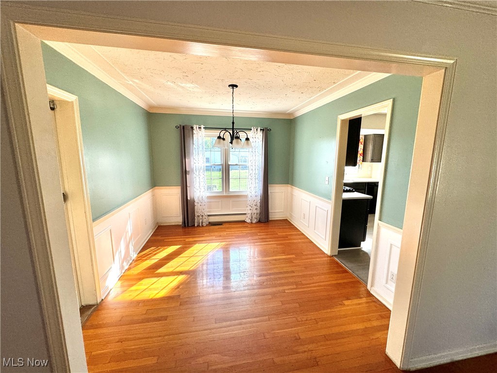 Unfurnished dining area with a textured ceiling, light hardwood / wood-style flooring, a notable chandelier, crown molding, and baseboard heating