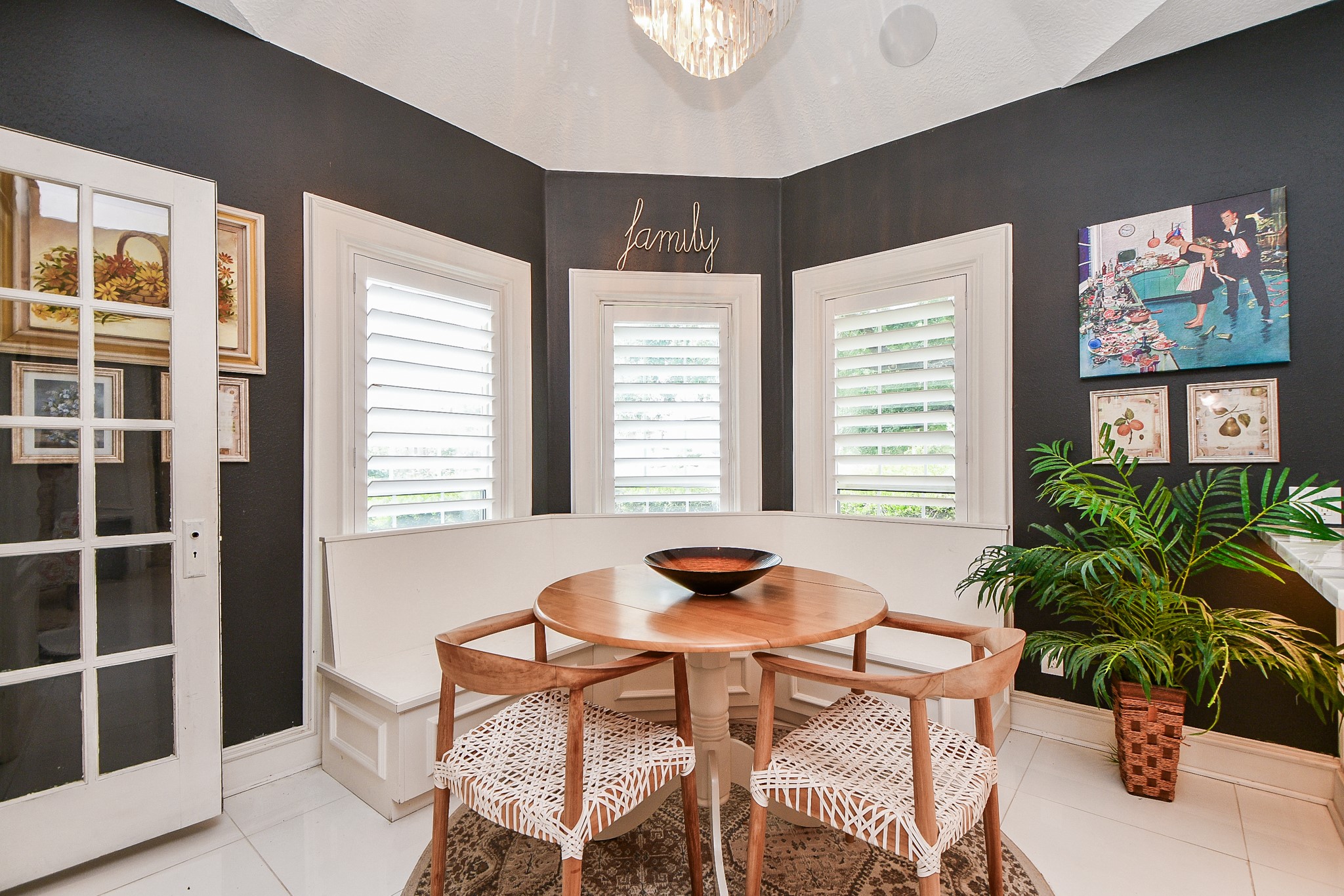 263 Wood Loop Street Houston, TX 77015 - Photo 35 of 45 This cozy breakfast nook features a round wooden table with woven chairs, set against a backdrop of dark walls and large windows with white shutters. A built-in bench provides additional seating, and decorative artwork and a plant add charm. The space is well-lit and inviting, perfect for casual dining.
